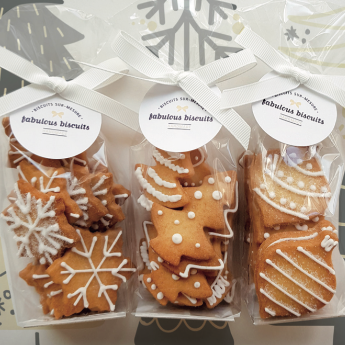 Biscuits de Noël emballés par lots, décorés de glaçage blanc en forme de flocons, sapins et boules.