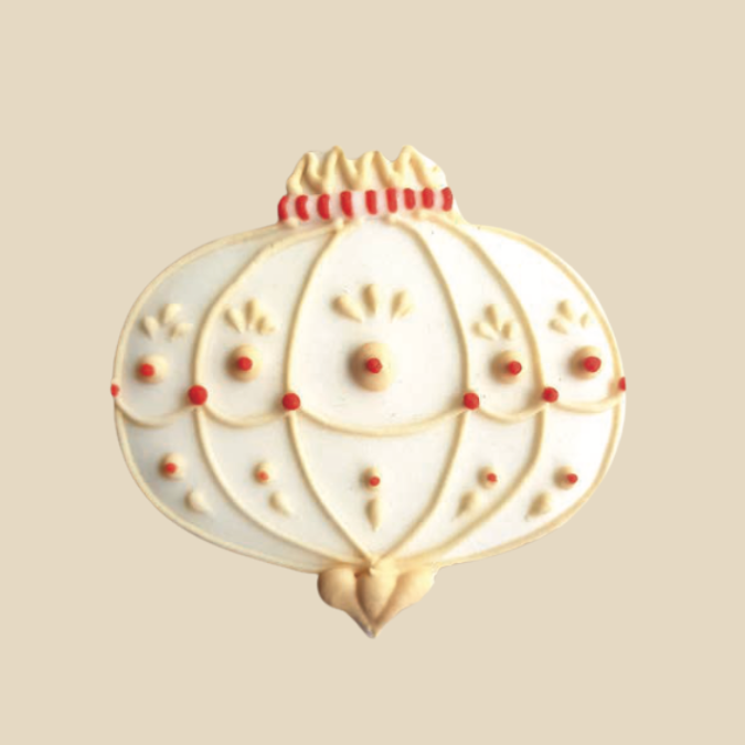 Biscuit en forme de boule de Noël blanche décorée de motifs fins et de pois rouges.