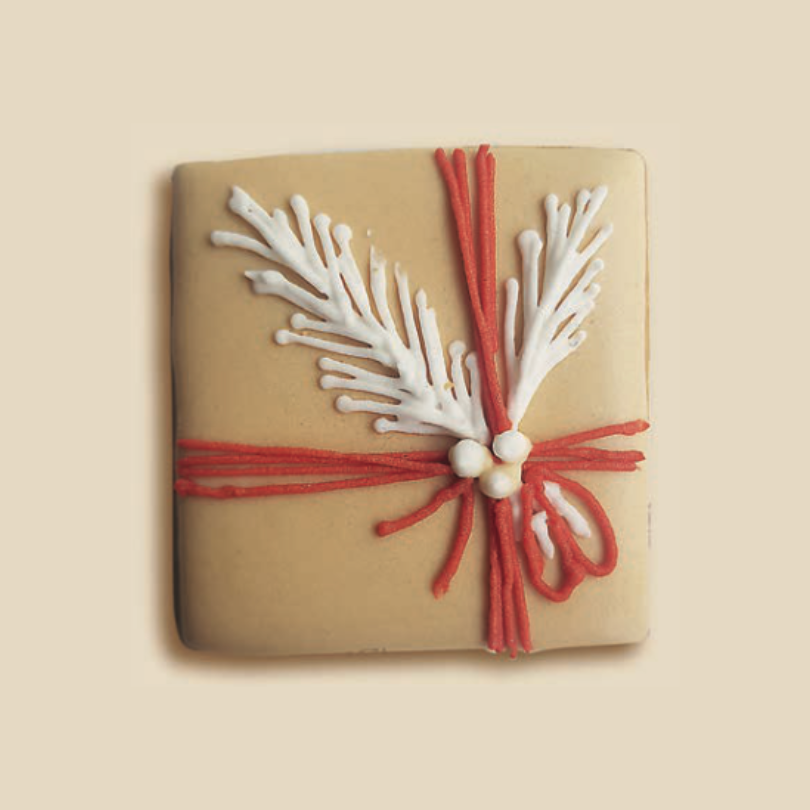 Biscuit carré décoré comme un paquet cadeau, avec branches de pin en glaçage blanc et ruban rouge.