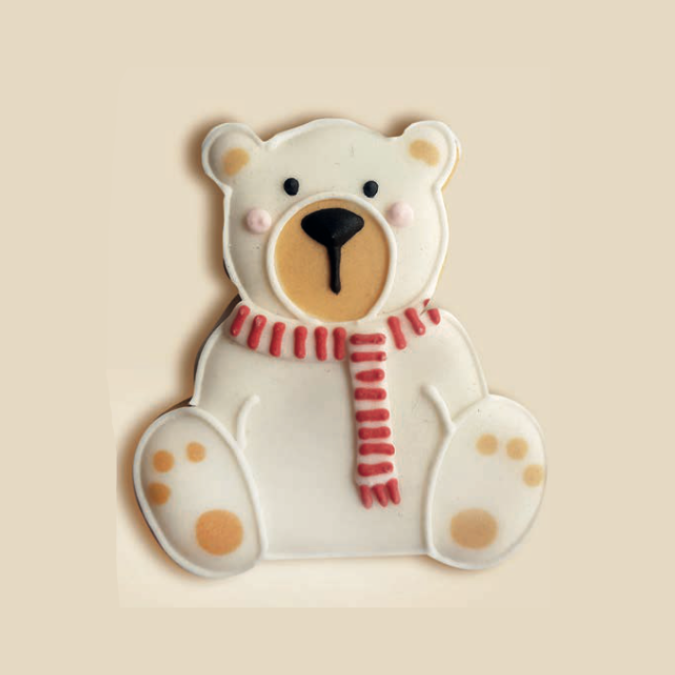Biscuit en forme d’ours blanc avec écharpe rouge, décoré au glaçage sur fond beige.