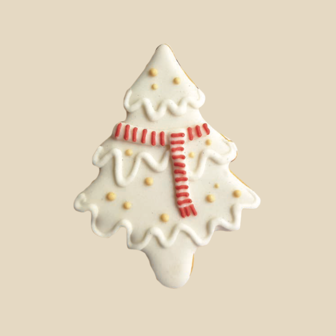 Biscuit en forme de sapin de Noël décoré de glaçage blanc, pois jaunes et écharpe rouge.