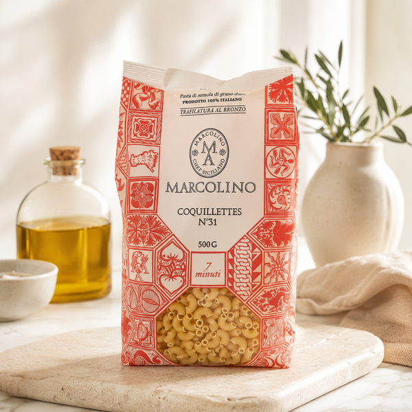 Pâtes coquillettes italiennes Marcolino en sachet 500 g, emballage rouge et blanc, présentées avec huile d’olive et décor cuisine.