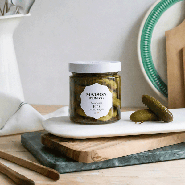 Bocal de cornichons fins Maison Marc, étiquette blanche élégante, posé sur planche en bois clair.