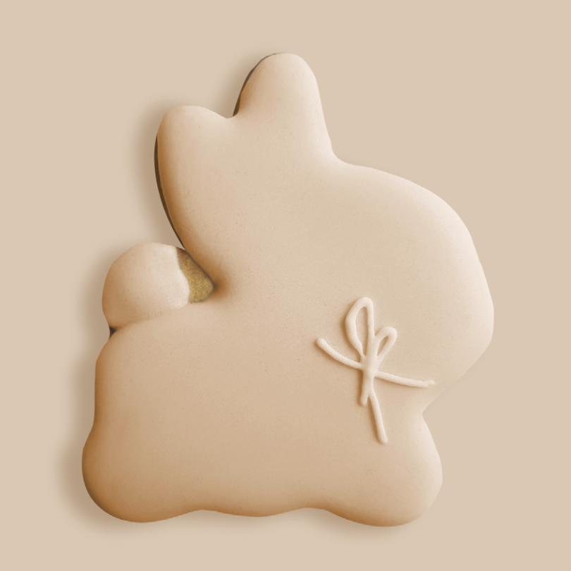 Biscuit en forme de lapin, recouvert d'un glaçage beige lisse et orné d'un nœud décoratif en glaçage blanc.