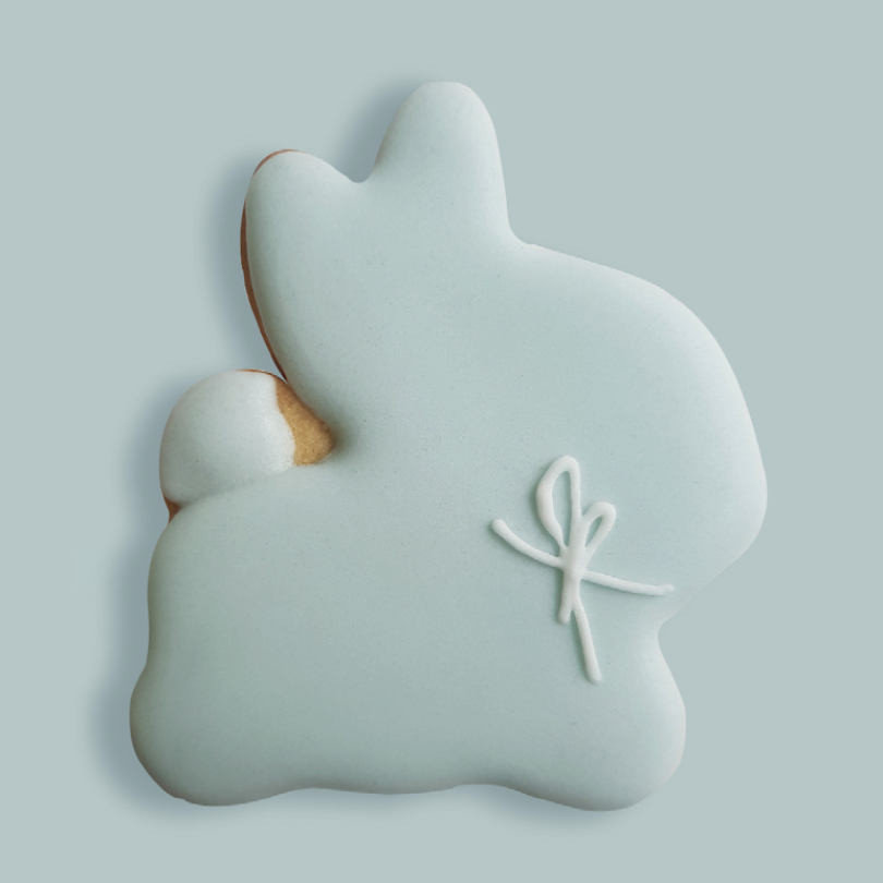 Biscuit en forme de lapin, nappé d'un glaçage bleu pastel et décoré d'un joli nœud blanc. 