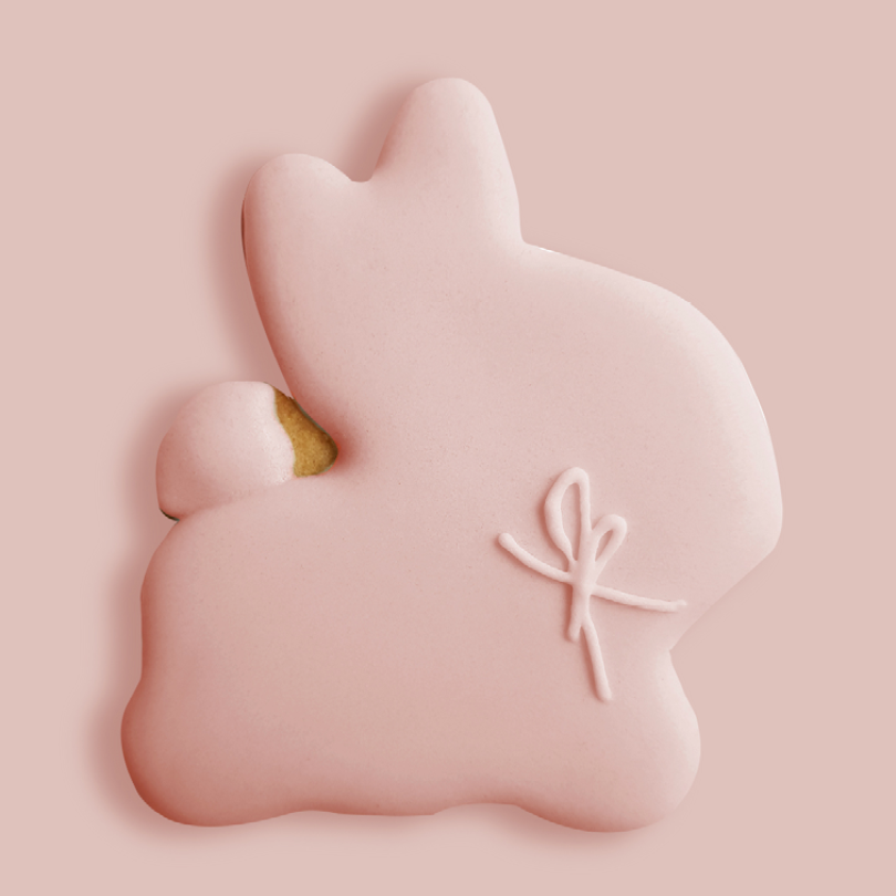 Biscuit en forme de lapin, recouvert d'un glaçage rose doux et orné d'un nœud en glaçage blanc. 