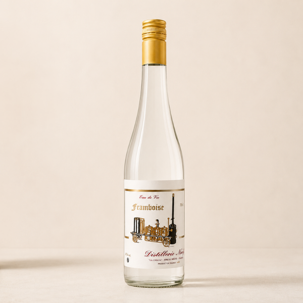 Eau-de-vie de framboise en bouteille transparente, capsule dorée et étiquette illustrée d’alambic, présentée sur fond beige épuré.