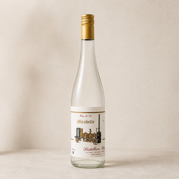 Eau-de-vie de mirabelle en bouteille transparente, capsule dorée et étiquette illustrée d’alambic traditionnel, sur fond clair épuré.