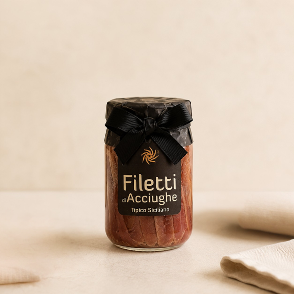 Filets d’anchois siciliens en bocal verre, présentation artisanale avec ruban noir sur fond épuré.