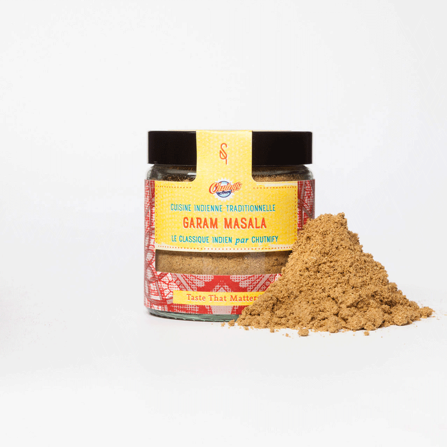 Pot en verre contenant du Garam Masala bio, un mélange d'épices traditionnel de la cuisine indienne. L'étiquette jaune et rouge, ornée de motifs vibrants, met en avant "Le classique indien par Chutnify". Une pile de poudre brun clair est disposée à l'avant, illustrant la texture fine et aromatique du mélange. Le slogan "Taste That Matters" figure en bas de l'étiquette.