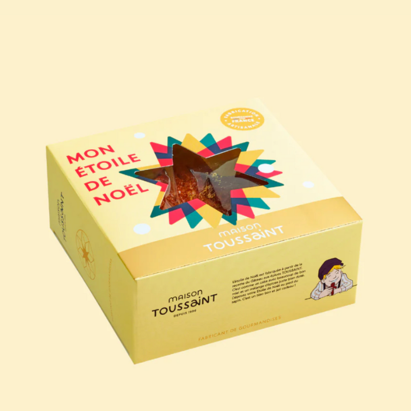Gâteau d'épices en forme d’étoile Maison Toussaint dans une boîte jaune festive, avec fenêtre transparente et décor coloré.