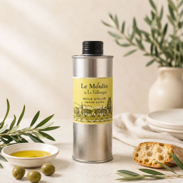 Huile d’olive vierge extra biologique Le Moulin de La Vallongue, bidon métallique argenté sur table claire avec olives et pain artisanal.