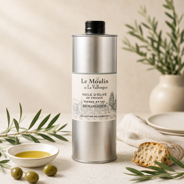 Huile d’olive biologique Le Moulin de La Vallongue, bidon argenté élégant sur table claire, ambiance méditerranéenne avec pain et olives.