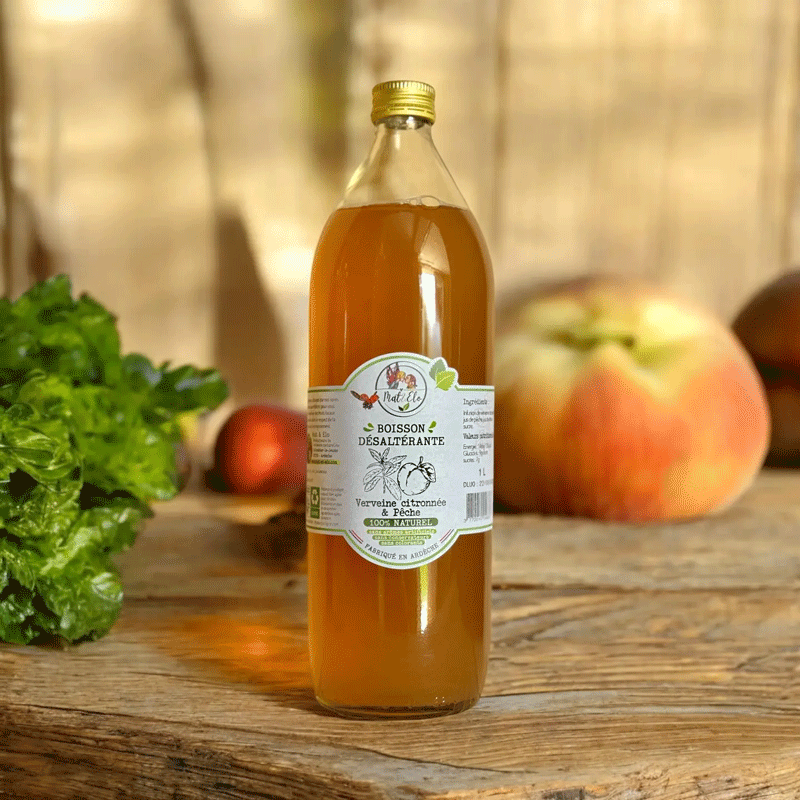 Bouteille en verre d’infusion glacée à la verveine citronnée et à la pêche, de marque Mat&Elo. L’étiquette blanche indique ‘Boisson désaltérante, 100% naturelle, fabriquée en Ardèche’. Le liquide est d’une teinte ambrée. La bouteille est posée sur une surface en bois, avec en arrière-plan une pêche mûre, des feuilles vertes et un décor naturel aux tons chaleureux.