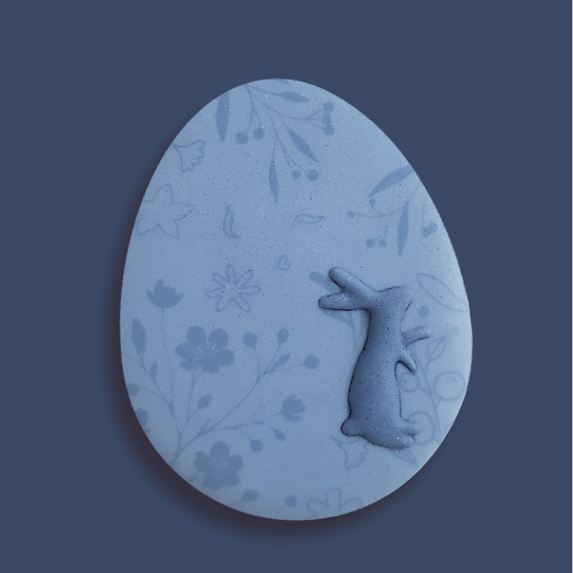 Biscuit de Pâques en forme d'œuf bleu, décoré avec un lapin en relief et des motifs floraux délicats. 