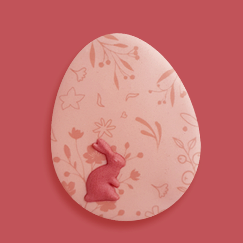 Biscuit de Pâques en forme d'œuf rose, décoré avec un lapin assis en relief et des motifs de fleurs et de feuilles.