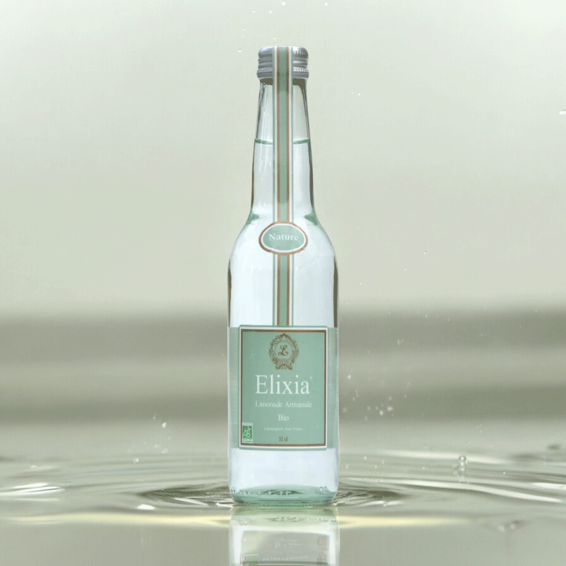 Bouteille de limonade artisanale bio Elixia nature, transparente avec étiquette verte sur fond d’eau.
