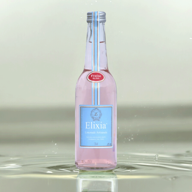 Bouteille de limonade artisanale Elixia à la fraise des bois, rosée, sur fond d’eau claire.