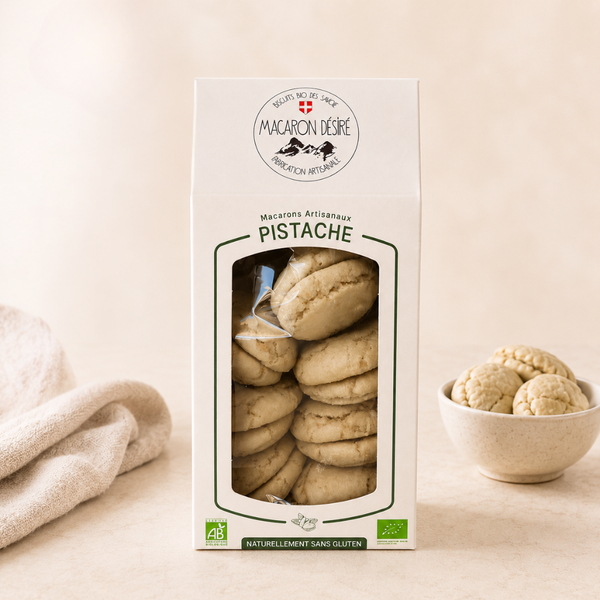 Boîte de macarons artisanaux à la pistache, de fabrication française et certifiée bio, naturellement sans gluten. Les macarons sont visibles à travers une fenêtre transparente sur le devant de l'emballage.