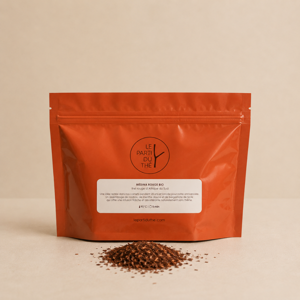 Thé rouge bio Médina Rouge en sachet orange avec rooibos en vrac sur fond clair.
