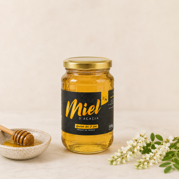 Pot de miel d’acacia en verre avec étiquette noire, accompagné d’une cuillère à miel et de fleurs d’acacia sur fond clair.
