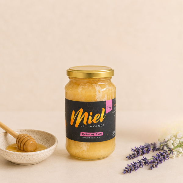 Pot de miel de lavande en verre avec étiquette noire, accompagné d’une cuillère à miel et de brins de lavande sur fond clair.