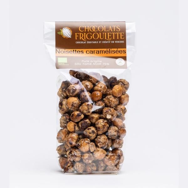 Noisettes caramélisées enrobées de chocolat noir 75 %, sachet transparent Chocolats Frigoulette sur fond clair.