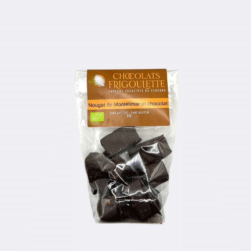 Un sachet transparent Frigoulette contenant des morceaux de nougat de Montélimar enrobés de chocolat noir. L’étiquette marron et orange porte le logo Chocolats Frigoulette et mentionne "Nougat de Montélimar et chocolat" ainsi que "Sans lactose - Sans gluten - Bio". Les morceaux de nougat au chocolat sont visibles à travers le sachet, avec une texture brillante et appétissante.