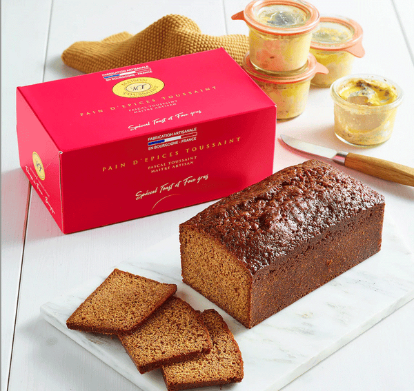 Pain d'Épices Spécial Toast & Foie Gras tranché sur une planche en marbre, avec boîte rouge et verrines de foie gras.