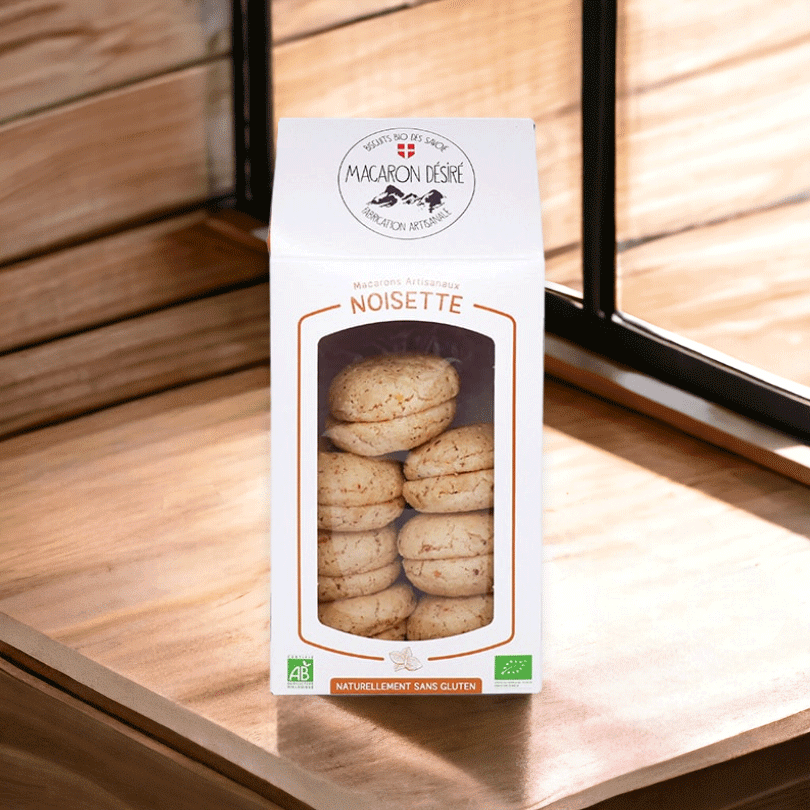 Boîte de macarons artisanaux à la noisette, de fabrication française et certifiée bio, naturellement sans gluten. Les macarons sont visibles à travers une fenêtre transparente sur le devant de l'emballage.