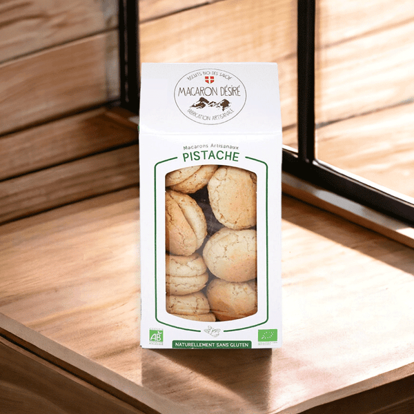 Boîte de macarons artisanaux à la pistache, de fabrication française et certifiée bio, naturellement sans gluten. Les macarons sont visibles à travers une fenêtre transparente sur le devant de l'emballage.