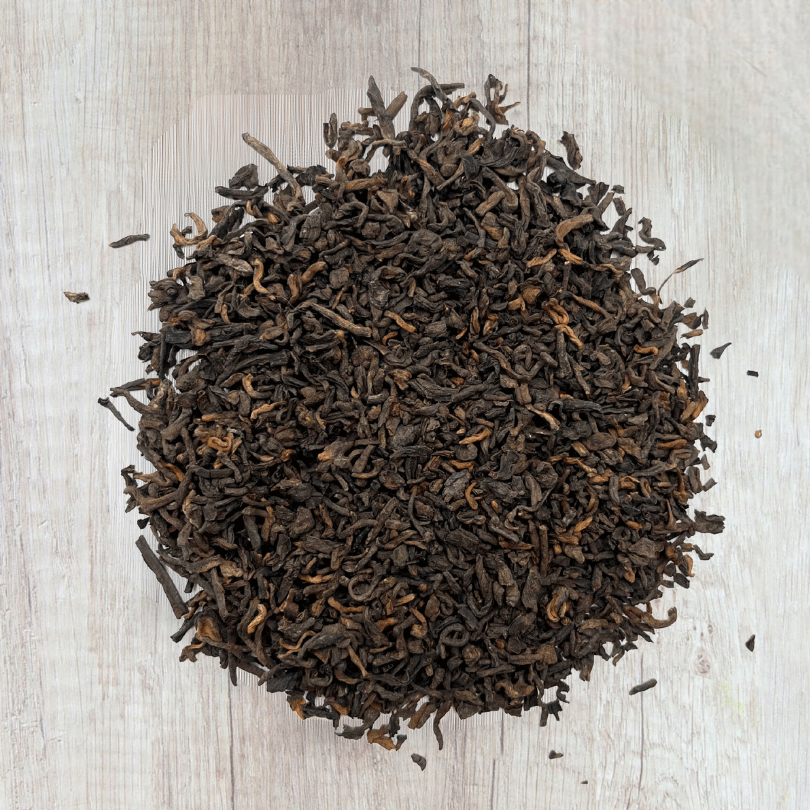 Tas de feuilles de thé sombres, torsadées et compactes, aux nuances brun foncé et quelques reflets ambrés. La texture dense et l’aspect vieilli caractérisent ce thé fermenté traditionnel chinois. 