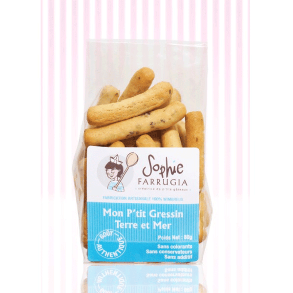 Sachet transparent de petits gressins "Mon P’tit Gressin Terre et Mer" de la marque Sophie Farrugia, avec une étiquette bleue et blanche mentionnant "Sans colorants, sans conservateurs, sans additifs", posé devant un fond à rayures roses.