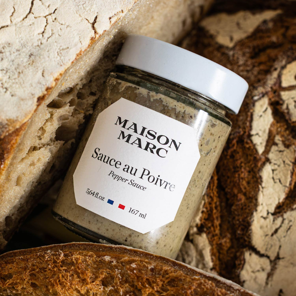 Sauce au poivre en bocal Maison Marc, texture crémeuse aux grains de poivre, mise en scène rustique avec pains artisanaux.