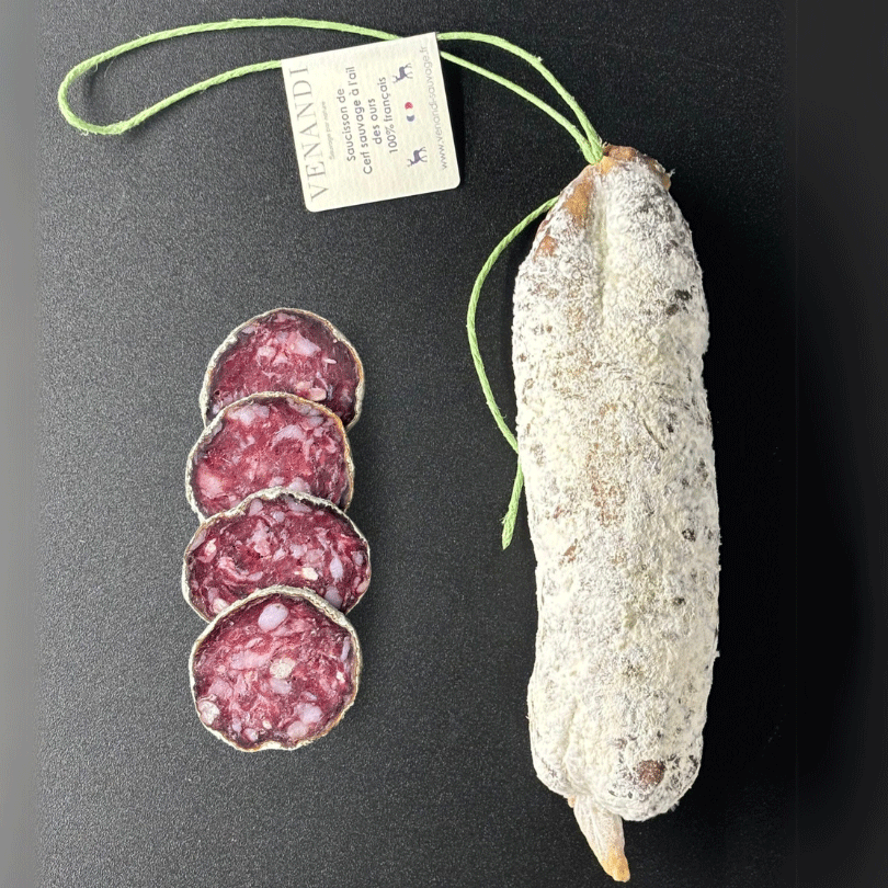 Un saucisson au cerf sauvage 100 % français, parfumé à l’ail des ours, repose sur un fond noir élégant. L’étiquette artisanale de la maison Venandi, attachée par une ficelle verte.
