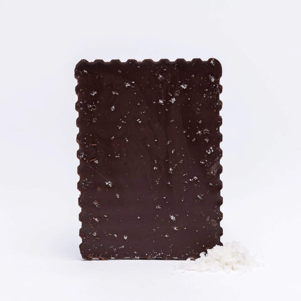 Tablette de chocolat noir 75% bio saupoudrée de fleur de sel, accompagnée d'un petit tas de sel disposé à côté.