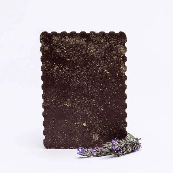 Tablette de chocolat noir 75% bio saupoudrée de fleurs de lavande, accompagnée d'un brin de lavande fraîche disposé à côté.