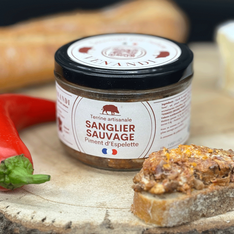Terrine de sanglier sauvage ouverte, avec tranche de pain, piment rouge et pain en arrière-plan.