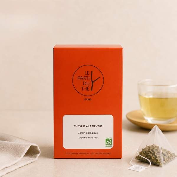 Boîte de thé vert bio à la menthe, avec sachet et tasse de thé en arrière-plan.