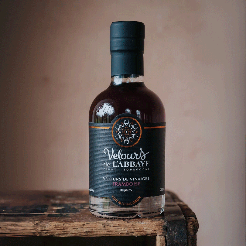 Bouteille de vinaigre à la framboise Velours de l’Abbaye sur une caisse en bois rustique.