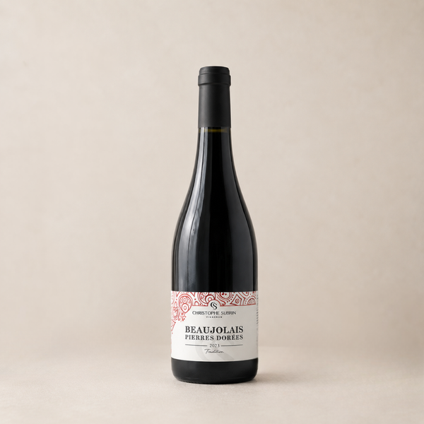 Bouteille de vin rouge Beaujolais Pierres Dorées 2023 Christophe Subrin, étiquette blanche et rouge, présentée sur fond beige épuré.