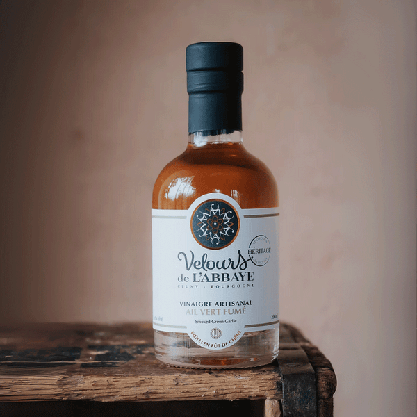 Bouteille de vinaigre à l’ail vert fumé sur une caisse en bois, étiquette blanche.