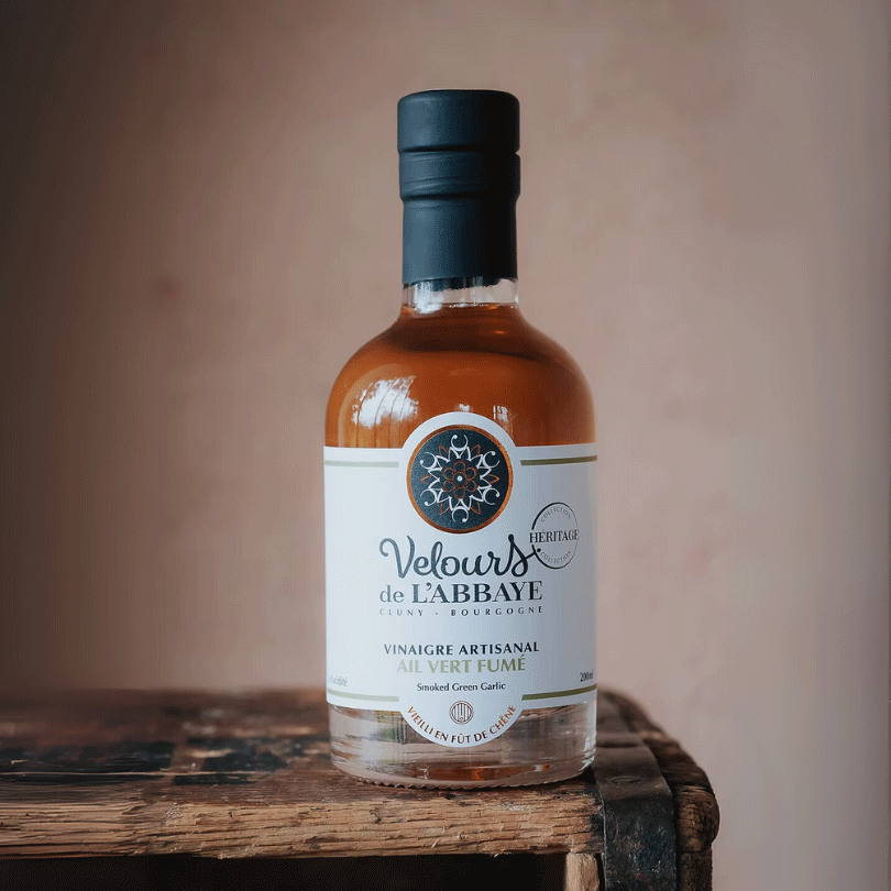 Bouteille de vinaigre à l’ail vert fumé sur une caisse en bois, étiquette blanche.