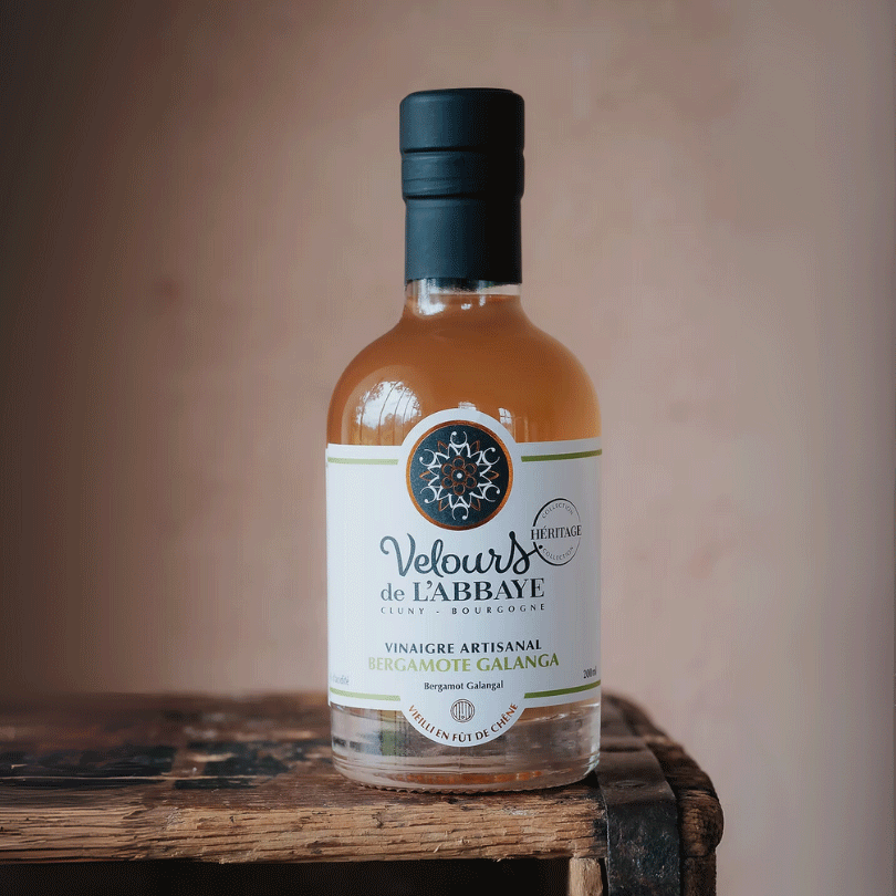 Bouteille de vinaigre bergamote galanga Velours de l’Abbaye posée sur une caisse en bois rustique.