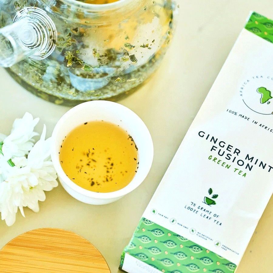 Tasse de thé infusé avec sachet Ginger Mint Fusion, théière transparente et fleurs blanches.