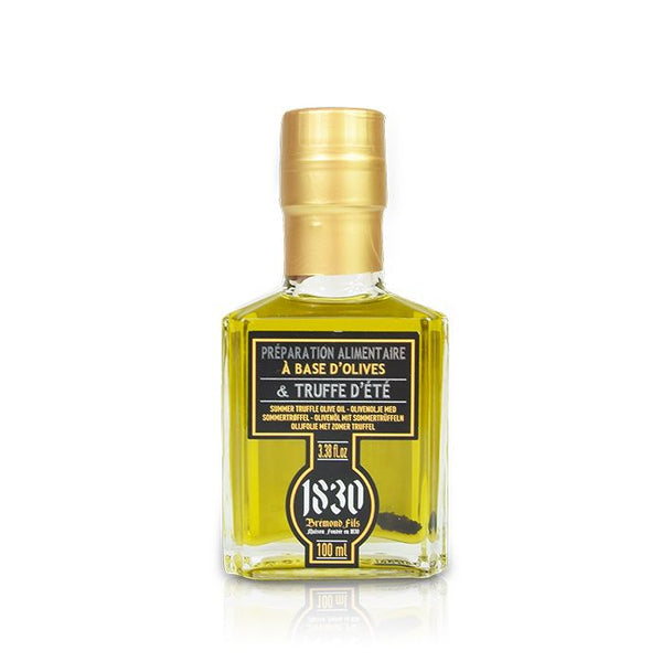 Bouteille d'huile d'olive à la truffe d'été de la marque 1830 Brémond Fils. Flacon en verre transparent laissant apparaître une huile dorée, avec une étiquette noire et dorée indiquant "Préparation alimentaire à base d'olives & truffe d'été".